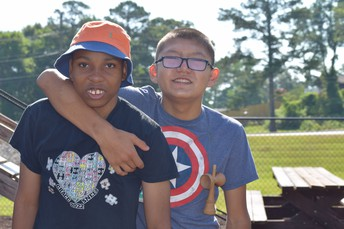 Two young boys smiling while outside at a camp.